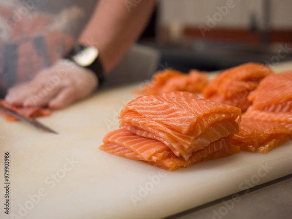 Fototapeta A Japanese cuisine master carefully slices fresh salmon into perfect portions. The special knife ensures each cut of salmon is even, while the chef's gloved hands highlight the precision of his work.