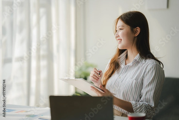 Obraz Businesswoman is calculating annual income and expenses at her office. Smiling female employee using laptop in modern office Copy space