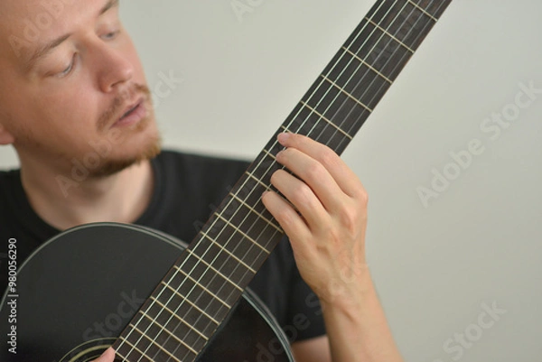 Fototapeta A man playing the guitar. Hands on the strings. Close-up portrait. Chord selection. Musician playing electric guitar. Banner wallpaper with copy space at the white background