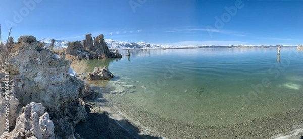 Obraz An extreme wide shot capturing the serene waters of Mono Lake on a calm, clear day. The lake's surface reflects the blue sky, with the bottom near the shore faintly visible through the clear water.