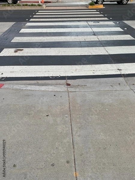 Obraz A clear midday view of a classic black-and-white striped crosswalk in Santa Monica, California. The sun casts minimal shadows, highlighting the textures of the worn crosswalk.