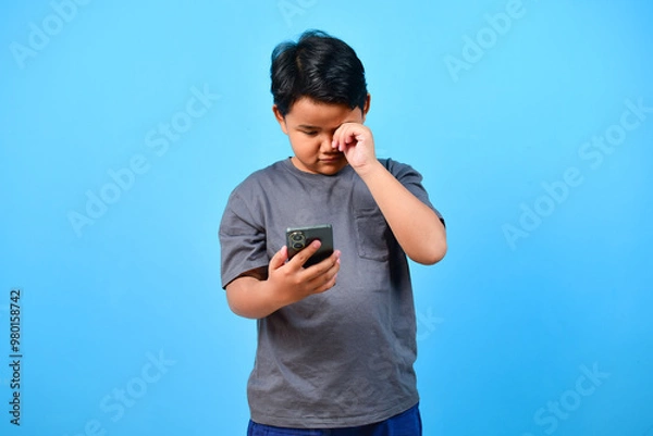 Obraz Child boy rubs his eyes for looking at phone. Hyperopia myopia astigmatism glaucoma and addiction to gadget
