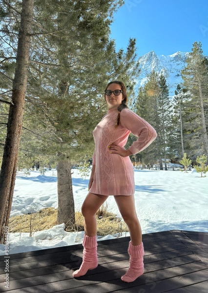 Obraz Woman in a pink outfit poses confidently amidst snow-covered scenery with mountains and pine trees in the background.