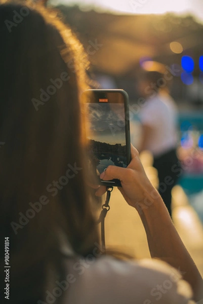Obraz Selective focus on modern cellular phone using for clicking pictures via camera, millennial woman tourist taking photos or shooting video via mobile phone during evening walk