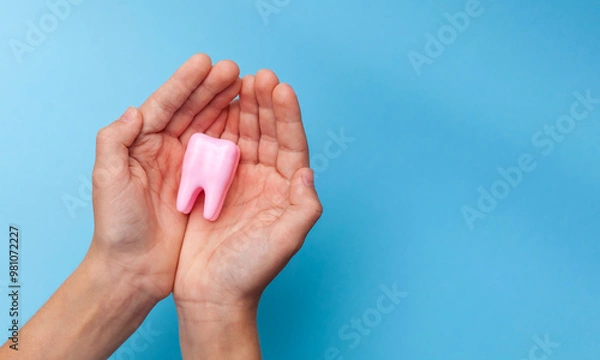 Fototapeta A hand holding a big tooth on a blue background. Concept of dental care. Teeth Clean and Oral Health. Taking care of yourself. Taking care of health. Close-up. Place for text.