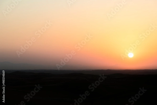 Fototapeta The desert at sunrise, showcasing a bright yellow-orange sky with plenty of copy space, making it a perfect background for text or creative work