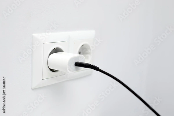 Fototapeta Closeup up of charger adapter plugged in power socket indoors. Concept of charging devices