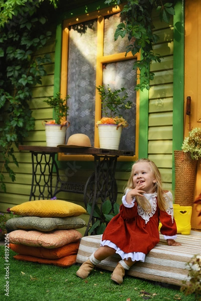 Obraz little girl sitting on a chair and looking at the camera. Little girl of two years old in a hat and a beautiful vintage dress. Beautiful little child walking in the garden