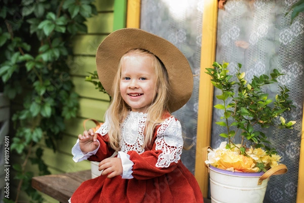 Obraz A little beautiful girl of two years old is walking in the yard. A little girl with blond hair and a hat