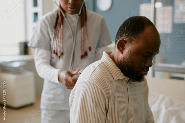Obraz Doctor using stethoscope for diagnosing African American man in medical examination room creating attentive and professional healthcare environment