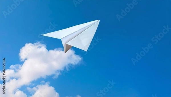 Fototapeta A white paper airplane soaring in a clear blue sky with soft clouds, representing creativity, freedom, and simplicity.