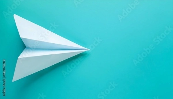 Fototapeta Minimalist photo of a white paper plane on a turquoise background. Perfect for themes of creativity, travel, and simplicity.