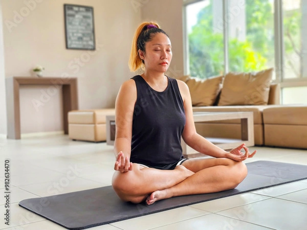 Obraz Asian woman doing sitting in yoga position sitting in lotus meditating at home. wellness concept
