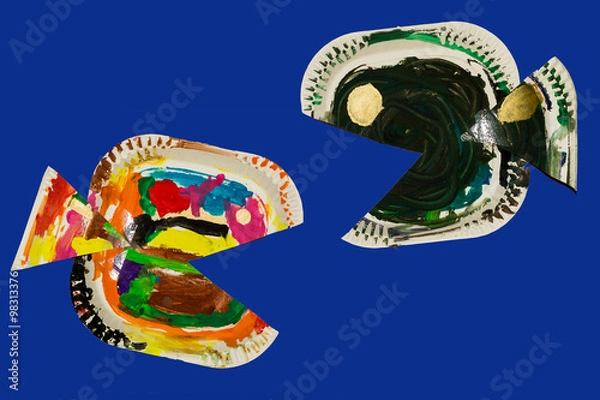 Fototapeta Fish made from paper plates and painted by child. Fish crafted by a child isolated against a blue background

