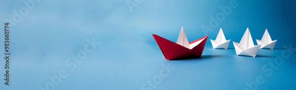 Fototapeta A group of white paper boats led by a red paper boat, Red paper boat leading white boats on a blue background, Business leadership concept
