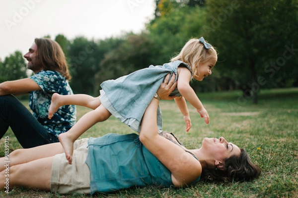 Obraz Happy young hipster family having fun while running, bowl,  rising up, piggyback ride their children in park on summer sunset
