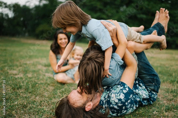 Obraz Happy young hipster family having fun while running, bowl,  rising up, piggyback ride their children in park on summer sunset
