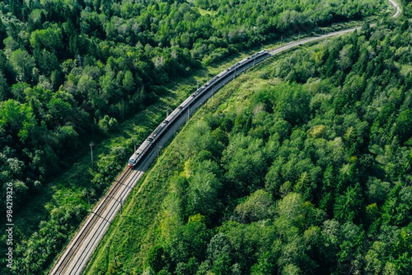 Fototapeta Aerial drone view of train in beautiful green summer forest. Long commuter train moving to railway station