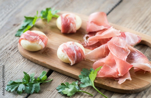 Fototapeta Mini cheese and prosciutto wraps on the wooden board