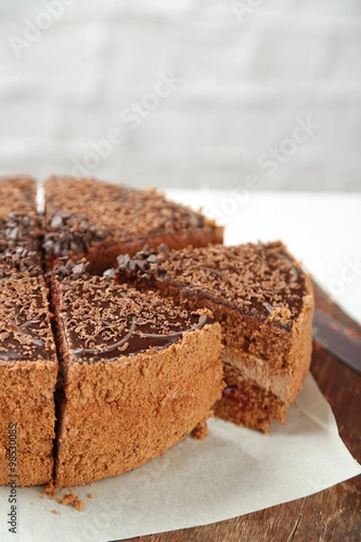 Fototapeta Sliced chocolate cake on wooden table, on light background