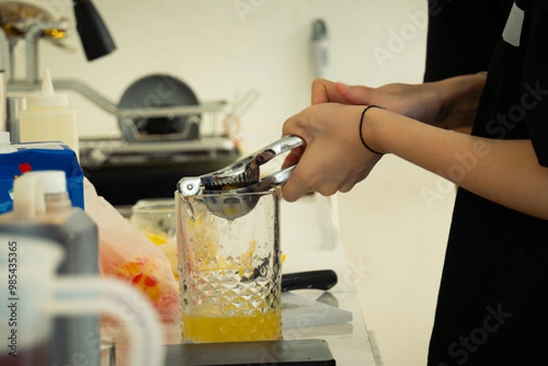 Fototapeta Women barista extracting lemon juice to glass using a lemon squeezer, in a cafe environment. Faceless portrait