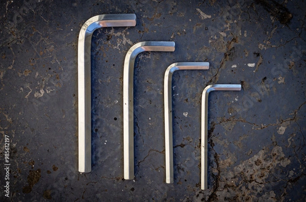 Fototapeta A set of steel hex keys arranged from large to small for assembly work on a dark gray cracked concrete surface. Color horizontal photo from top to bottom with a plain background.