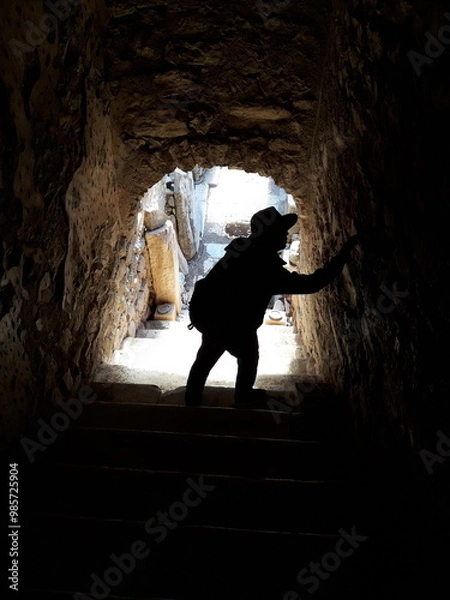 Obraz a man is standing in a cave with a shadow on the wall.
