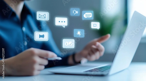 Fototapeta A businessman using a laptop with social media icons floating above.  The image represents communication, technology, and digital marketing.