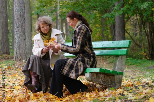 Fototapeta Mother and doughter sitting on a bench in autumn park