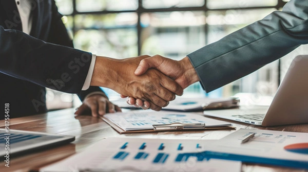 Obraz Financial advisor meeting with clients – formal meeting, papers and charts on the table, handshake between advisor and clients.