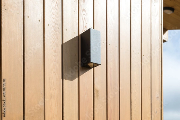 Fototapeta black front lamp on the wooden facade of the house on a sunny day