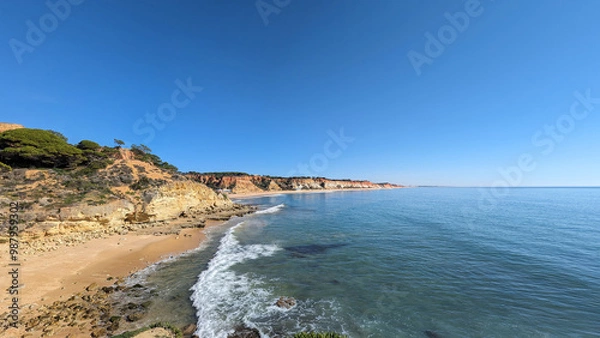 Fototapeta Summer weather on the beaches of the Algarve in Portugal with breaking waves, wet rocks in the sand and overgrown slopes on the coast