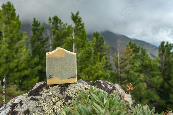 Fototapeta Piece of craft soap on the background of mountains, forests and sky. Concept of the image of organic cosmetics in a natural environment