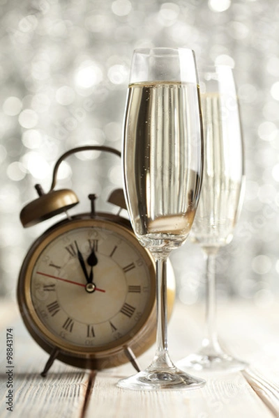 Fototapeta Glasses of champagne and alarm clock on wooden background