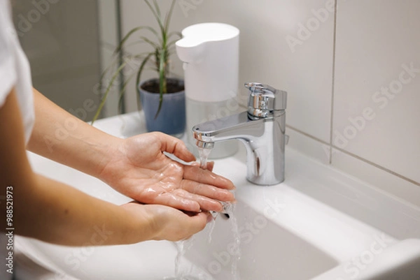 Fototapeta Female washing hands in bathroom sink at home checking temperature touching running water with hand
