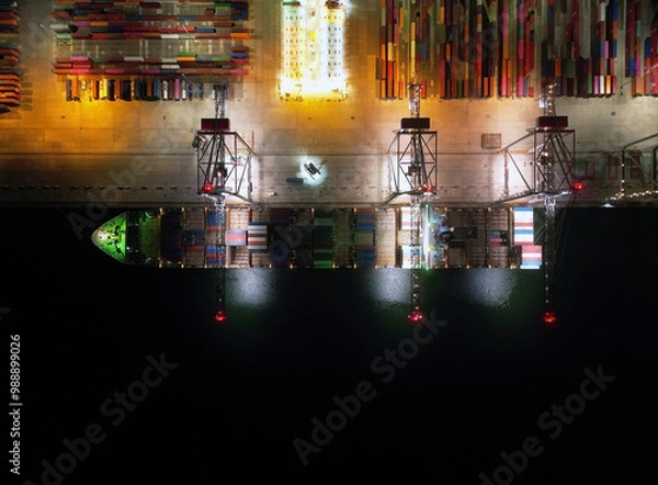 Fototapeta Aerial view of Industrial shipping port. View from drone. Loading containers on the ship, cranes load containers. Night shooting.