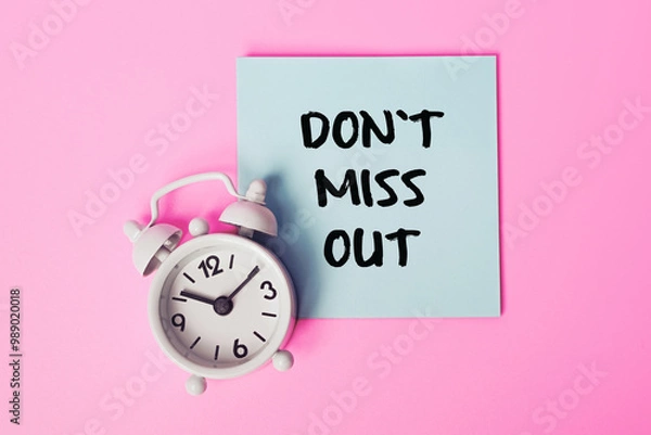 Fototapeta "Don't Miss Out" Written on a Sticky Note. Ideal for Marketing Promotions, Sales Campaigns, and Urgency Messaging. White alarm clock and Blue Note on a Pink Background
