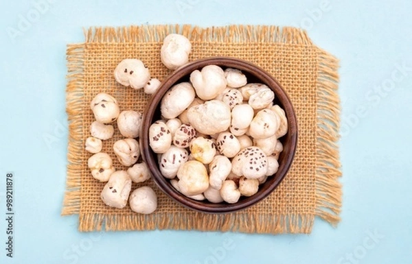 Obraz Top View of Makhana or Fox Nut in a Wooden Bowl on Burlap Fabric Isolated on Light Blue Background with Copy Space, Also Known as Lotus Seed Pop, Euryale Ferox or Gorgon Nut