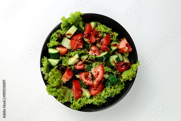 Fototapeta Vegetable salad of tomatoes, cucumbers, onions, lettuce dressed with aromatic dressing in a black plate on a white  background