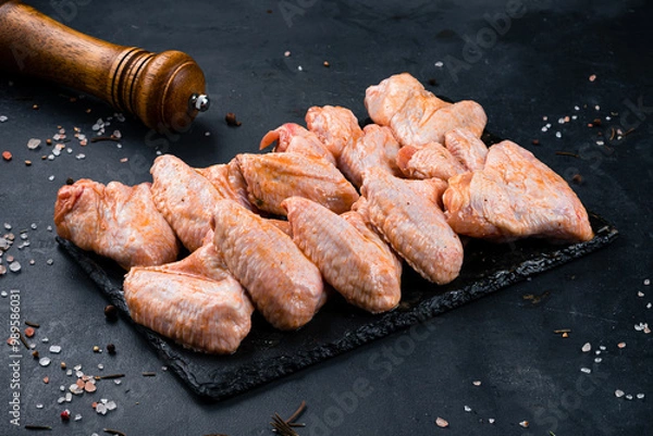 Fototapeta Raw marinated barbecue chicken wings in sauce and spices on a dark background.