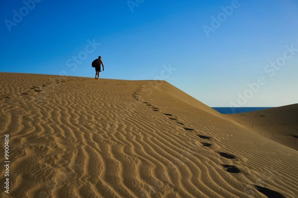 Fototapeta Lost man on sandy dunes in desert / Sandy and wavy dunes with stylish forms in a wide desert under blue sky