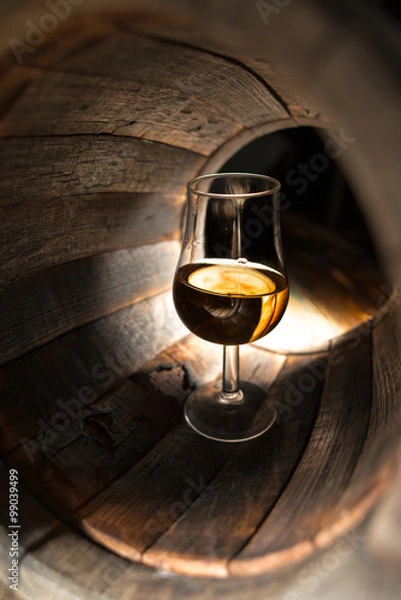 Fototapeta A glass of whiskey on a background of oak barrels