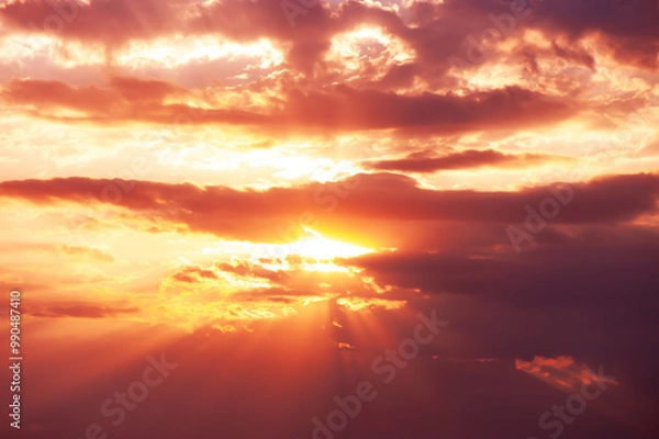 Fototapeta A dramatic sunset with glowing orange and pink light rays breaking through clouds, creating a stunning sky scene