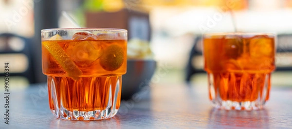 Fototapeta Deux verres de cocktail apéritif orange avec une olive et une pique à l'intérieur, posés sur une table de bar en extérieur et des chips à l'arrière plan par une fin de journée ensoleillée à Venise