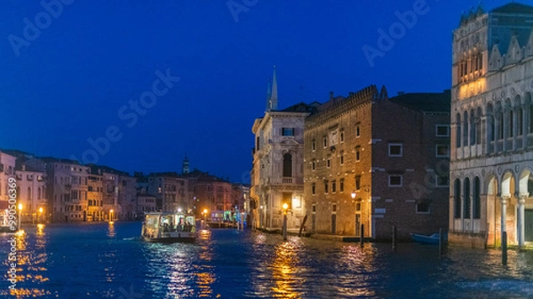 Fototapeta Vue de Venise de nuit depuis le Grand canal avec des quais éclairés et des bâtiments anciens, et le vaporetto qui navigue.
