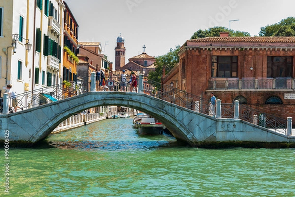 Fototapeta Pont sur un canal à Venise dans le quartier du Cannaregio par une journée ensoleillée avec un ciel bleu et des bâtiments anciens.