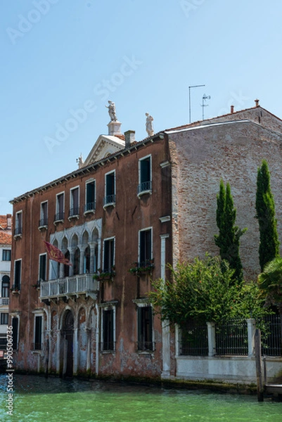 Fototapeta Maison traditionnelle rouge à Venise vue du grand canal avec un quai et un ciel bleu à l'arrière plan par une journée ensoleillée.