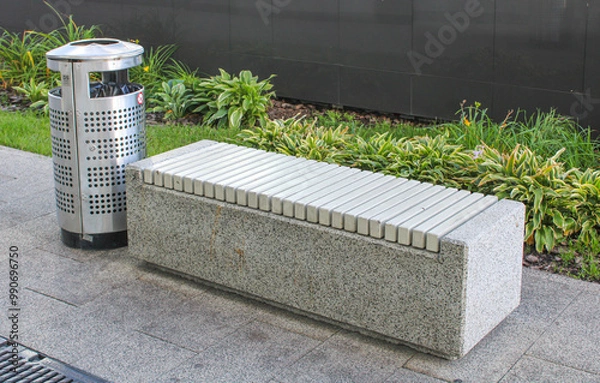 Fototapeta A concrete bench is next to a shiny stainless steel trash can