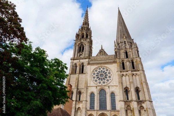 Fototapeta Chartres, France. The Cathedral, made of gray stone, features intricate carvings on the facade. A stunning rose window is flanked by smaller windows and statues of saints against a blue sky with