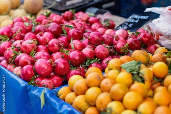 Obraz Bright red pomegranates rest alongside vibrant oranges at a bustling market, showcasing the rich colors and enticing variety of fresh fruits available for shoppers to enjoy.